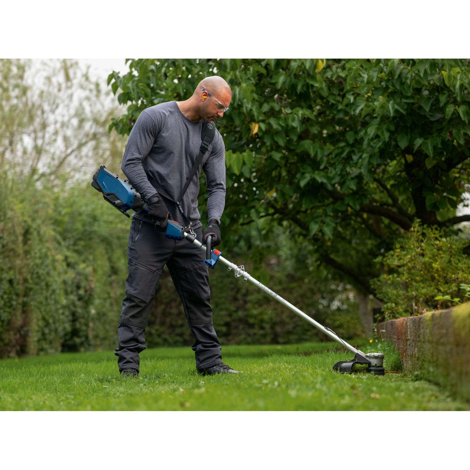 Mann trimmt Rasen mit dem Bosch Professional Akku-Rasentrimmer GRT 18V-40 Solo.