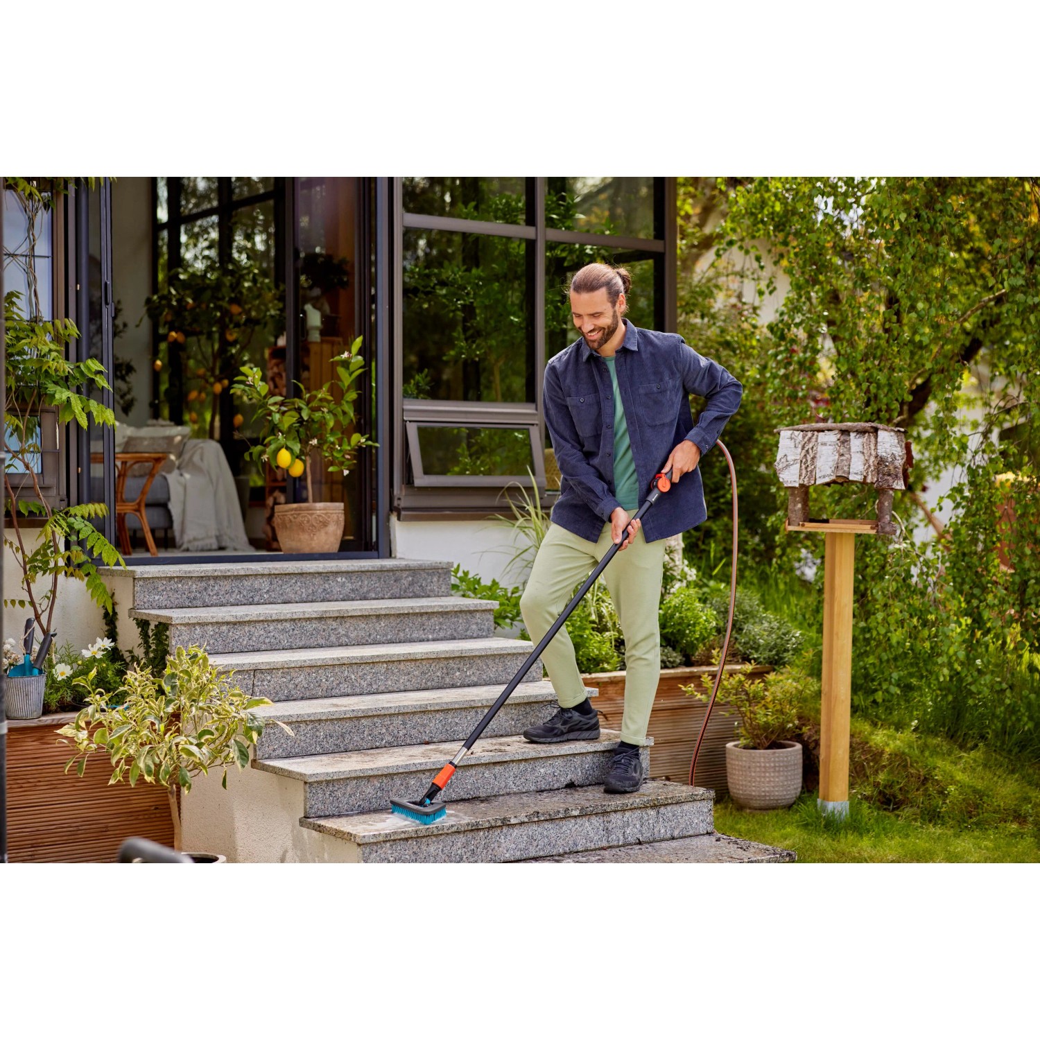 Mann reinigt Treppe mit Gardena Cleansystem Stielbürste Hard Flex in Anthrazit.