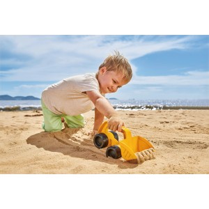 Gelber Hape Monster-Bagger aus Kunststoff im Sand, Kind spielt am Strand.