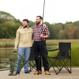 Zwei schwarze Sunula Campingstühle mit Getränkehalter, Angler mit Angel und Kescher am See.