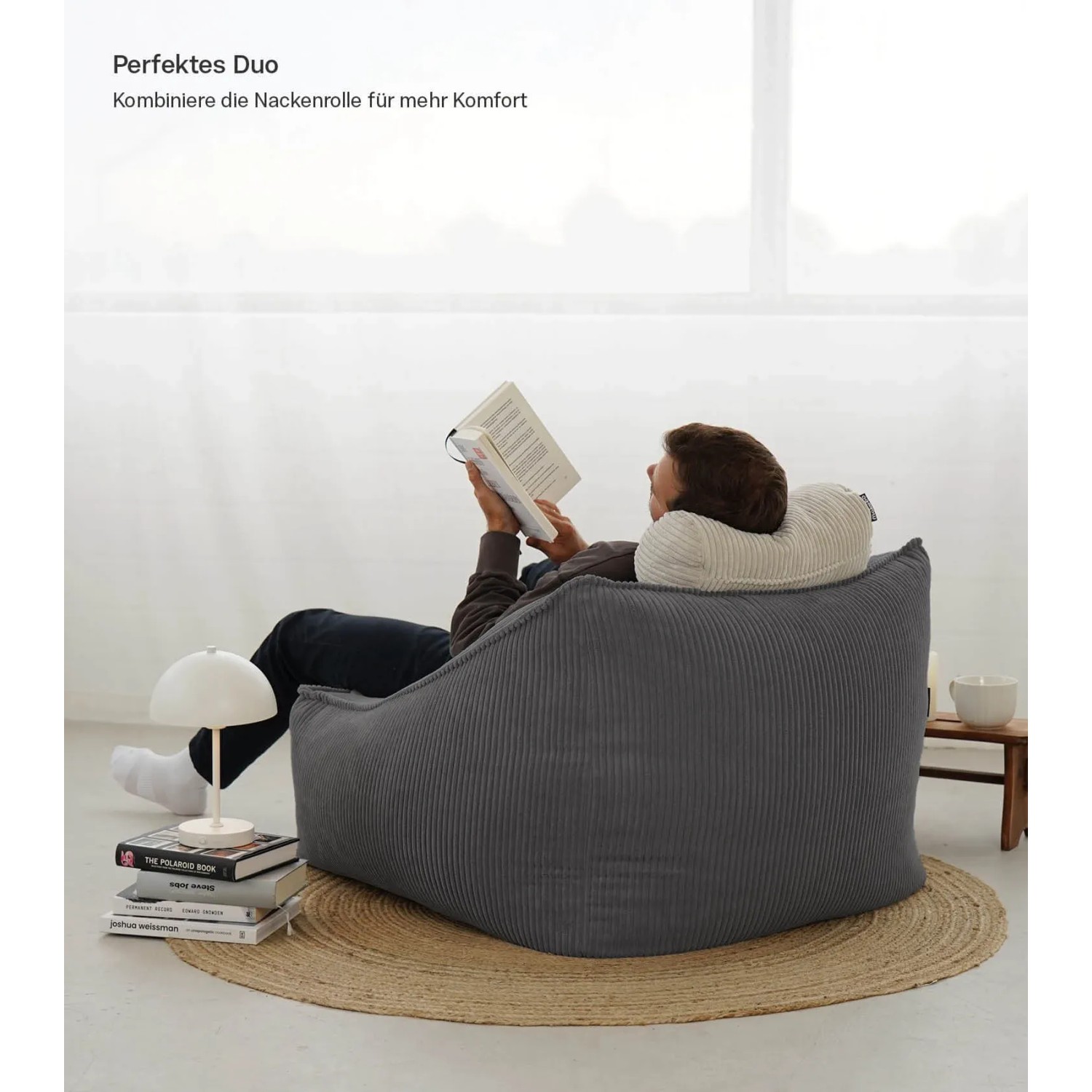 Grauer mokebo Cord Sitzsack Sessel "Der Lümmel" mit Hocker und lesendem Mann im Wohnzimmer.