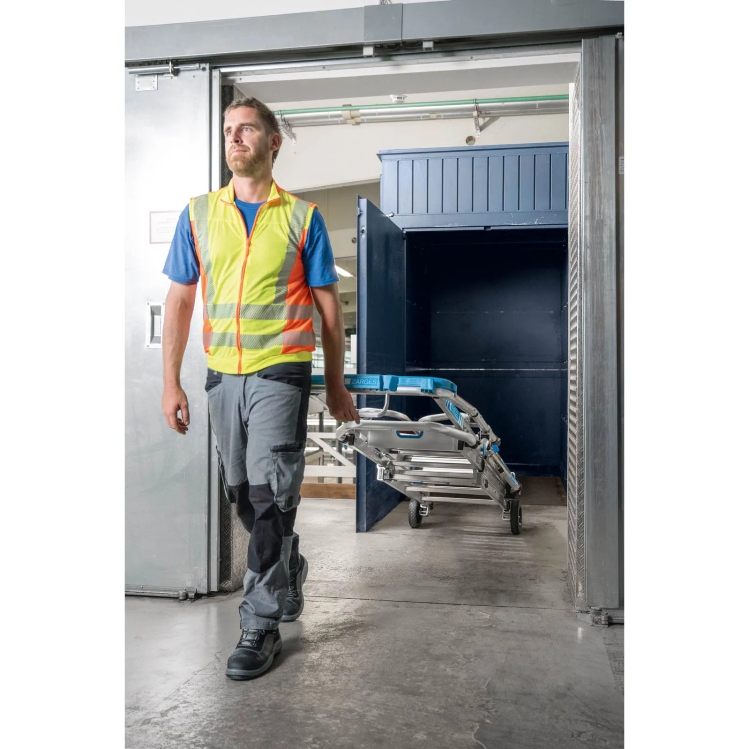 Mann trägt Zarges Teleskop Plattformleiter. Die Leiter ist zusammengeklappt und hat 8-12 Stufen.