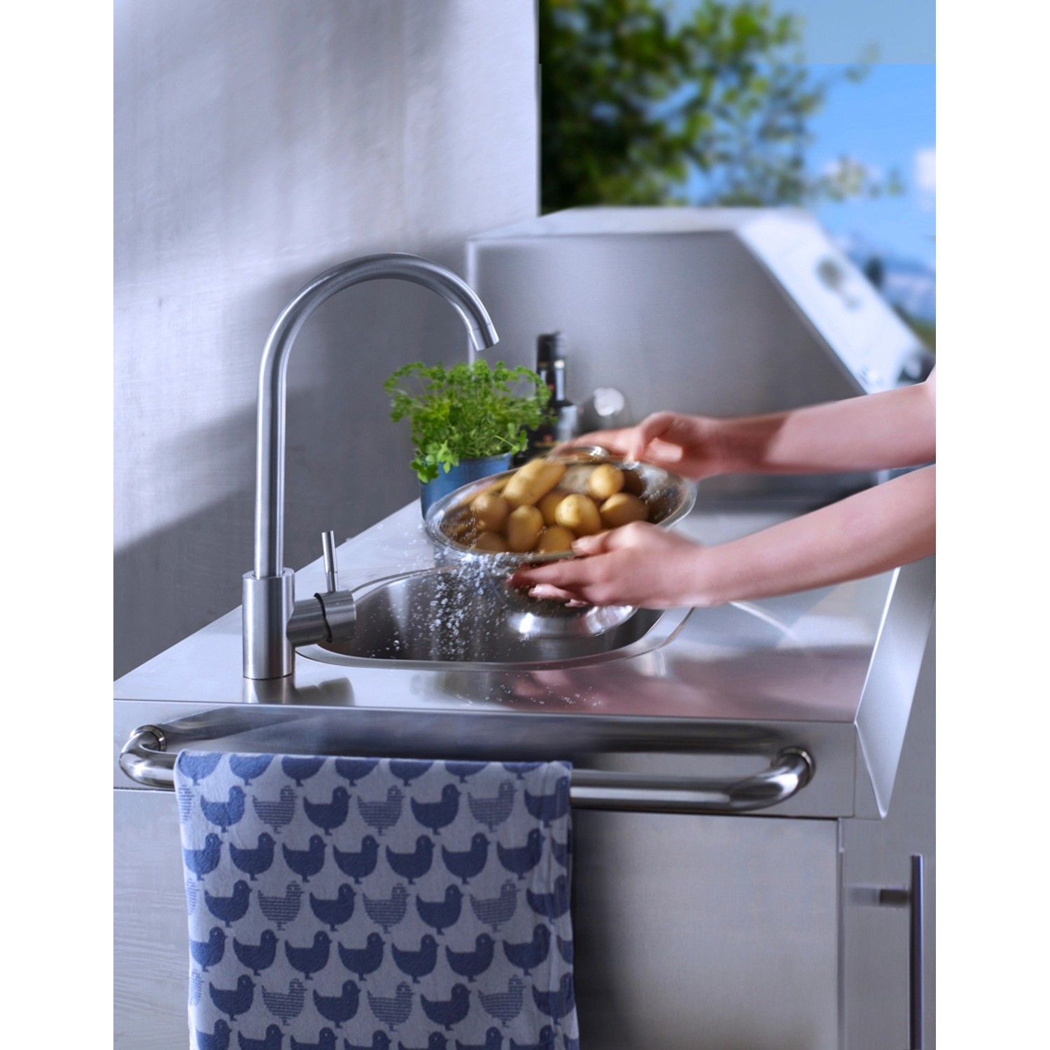 Spüle der Buschbeck Outdoorküche Oxford mit Person, die Kartoffeln wäscht.