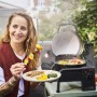 Frau mit Grillgut vor Char-Broil Elektrogrill Patio Bistro Cube E (schwarz).