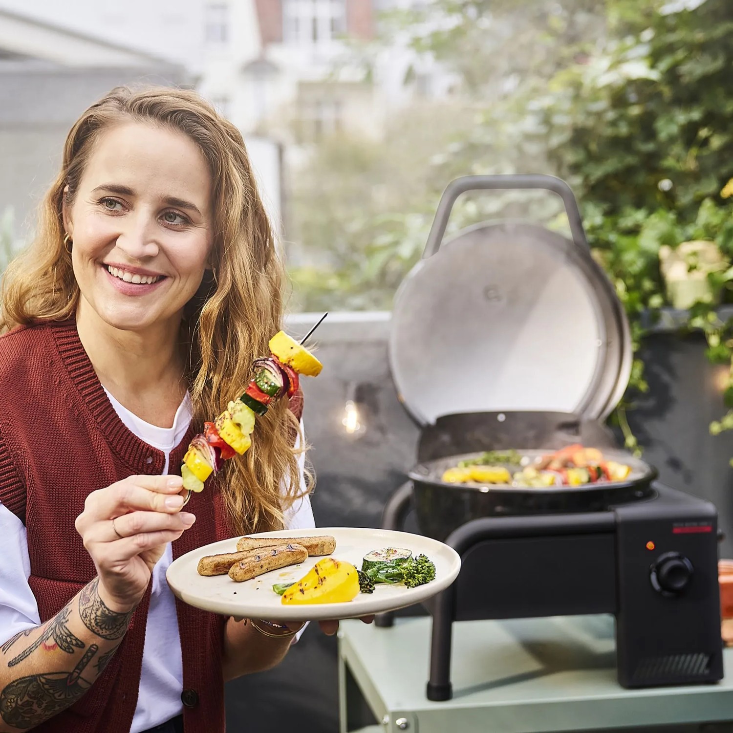 Frau mit Grillgut vor Char-Broil Elektrogrill Patio Bistro Cube E (schwarz).