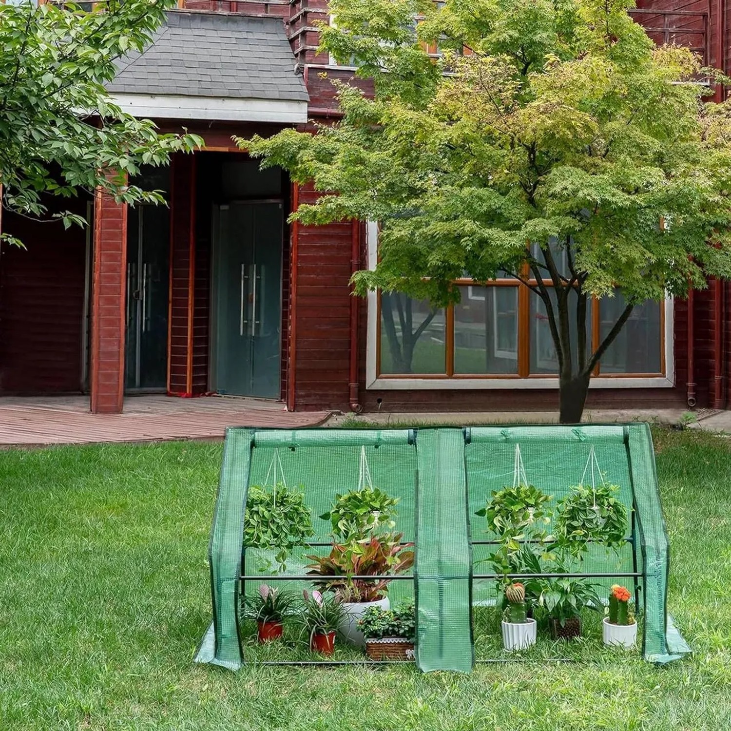 Grünes WOLTU Foliengewächshaus mit Metallrahmen, gefüllt mit Pflanzen, auf Rasen im Garten. Ideal für Anzucht & Schutz.