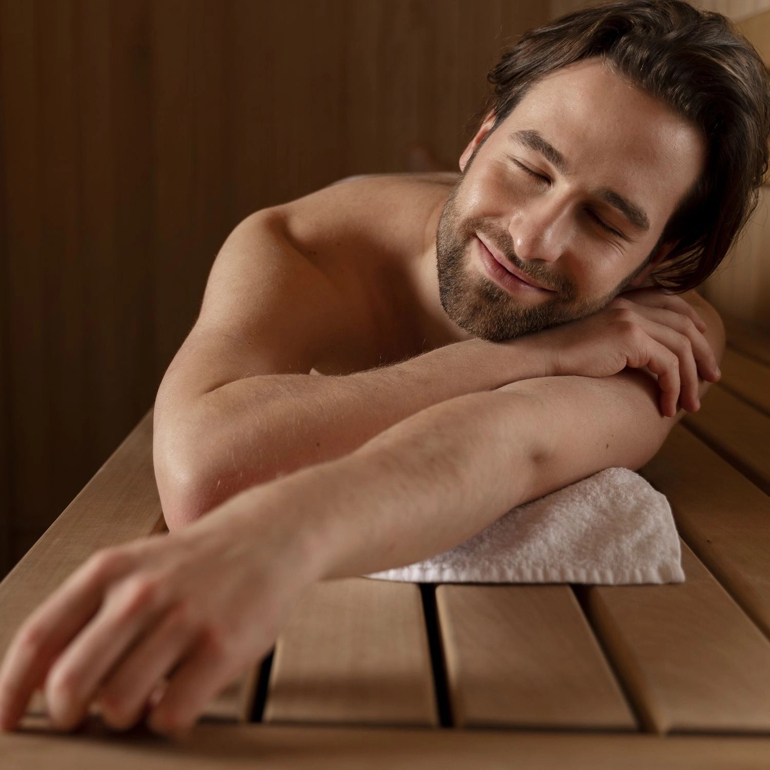 Entspannter Mann in Sauna auf Holzbank mit Handtuch. Wellness und Erholung.