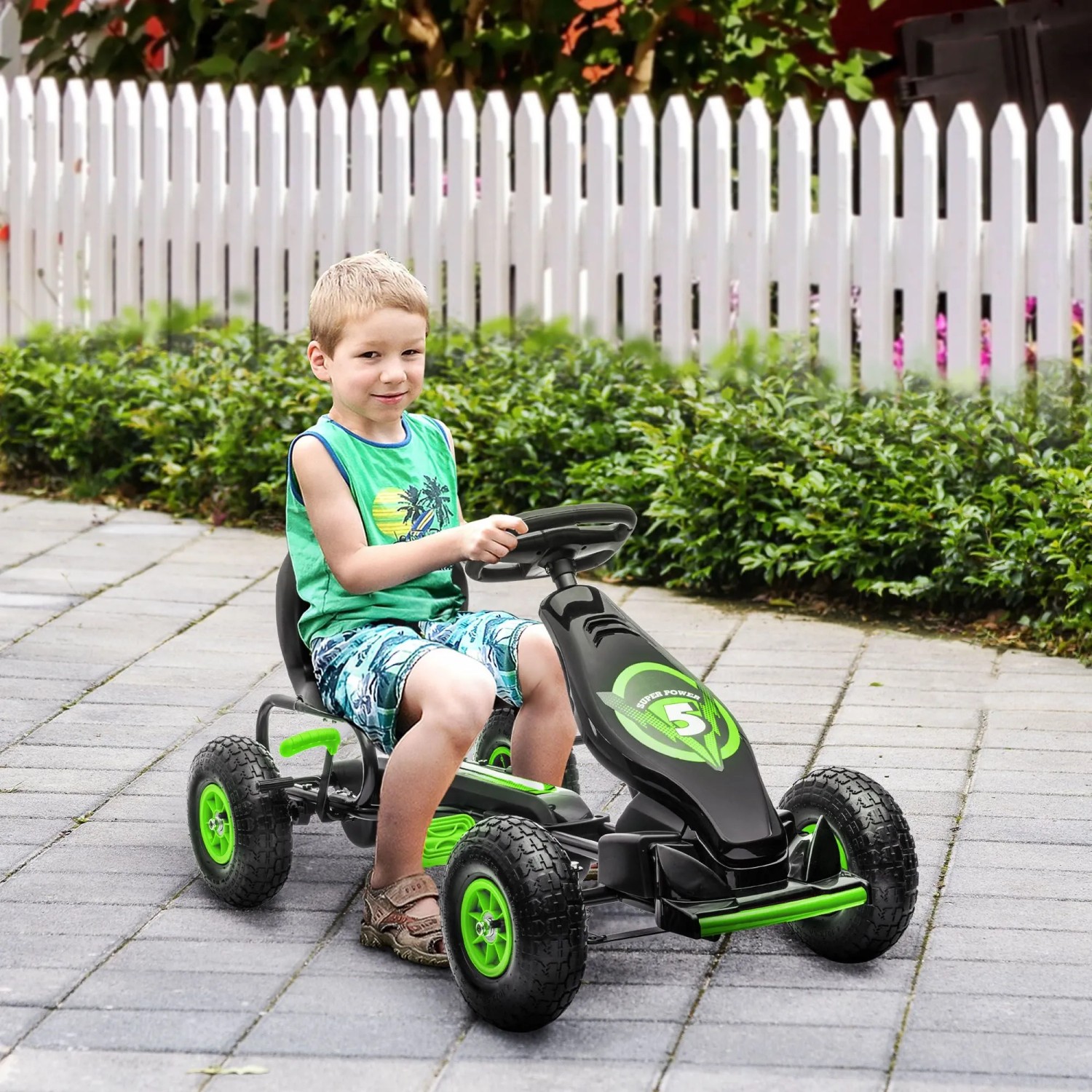 Lächelnder Junge fährt schwarzes HOMCOM Gokart mit grünen Akzenten und Pedalen auf gepflastertem Weg.