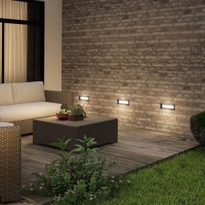 Moderne Lucande LED Außenwandleuchte Lachlain aus Alu an Ziegelwand. Beleuchtet Terrasse mit Holzdeck.