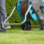 Gardena CleverRoll M Easy Schlauchwagen mit Schlauch auf Rasen, Fuß auf Standfuß.
