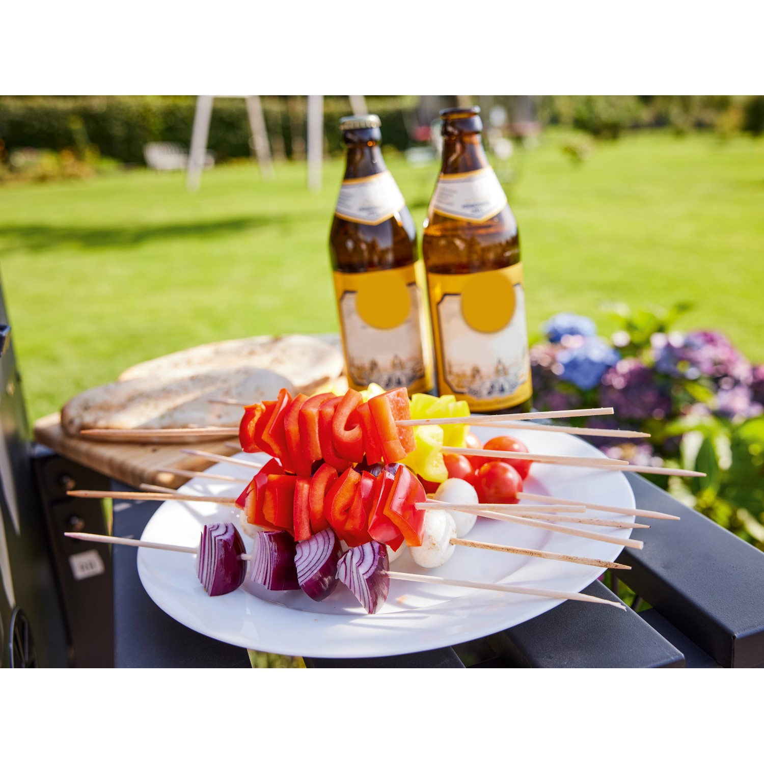 Grillspieße mit Gemüse und Brot auf Jamestown Holzkohlegrill Jaxon. Zwei Bierflaschen im Hintergrund.