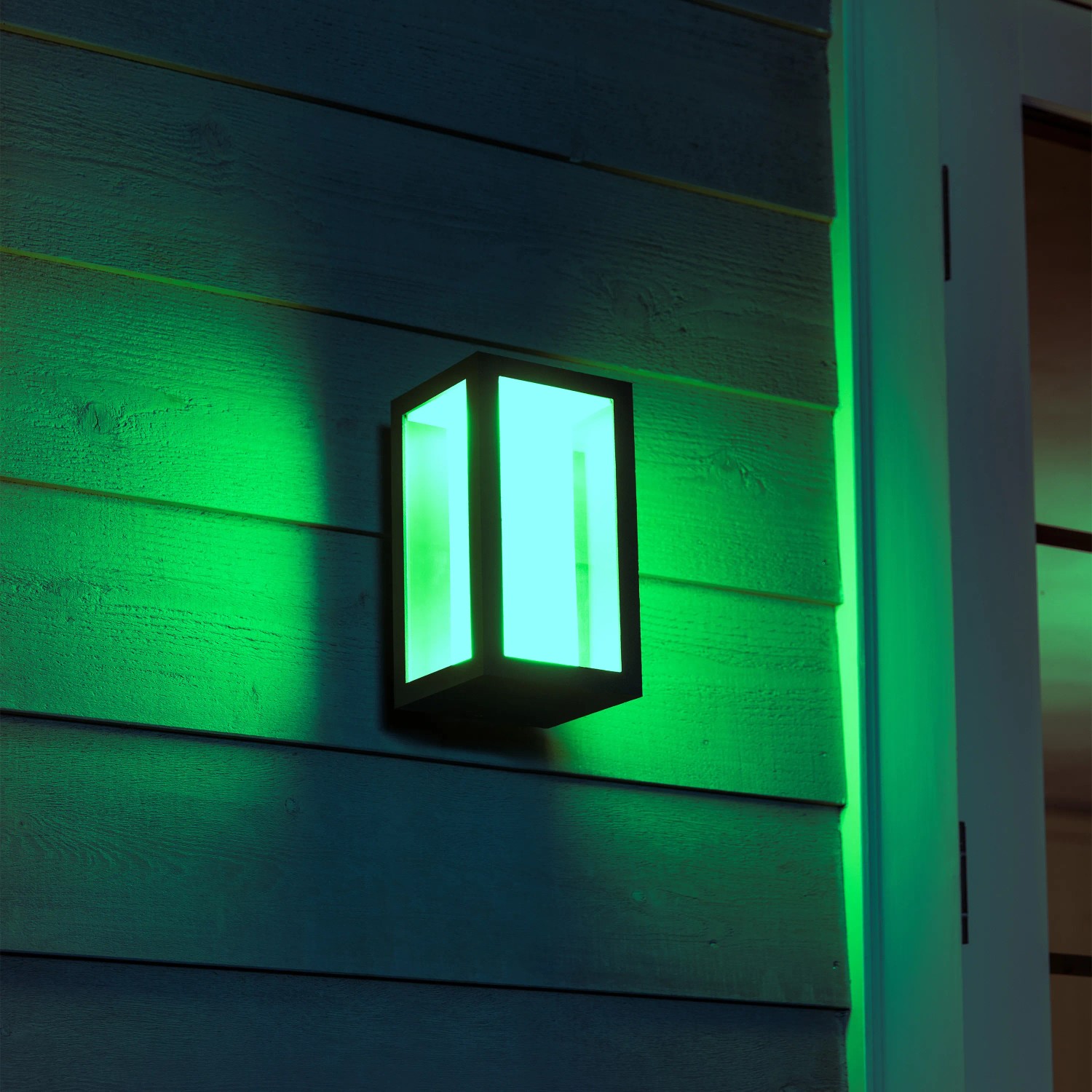 Smarte Philips Hue LED-Wandlampe Impress, schwarz, mit grünem Licht an Hauswand.