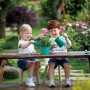 Zwei Kinder spielen mit dem Hape Gartenwerkzeug-Set (Gießkanne, Schaufel) im Garten.