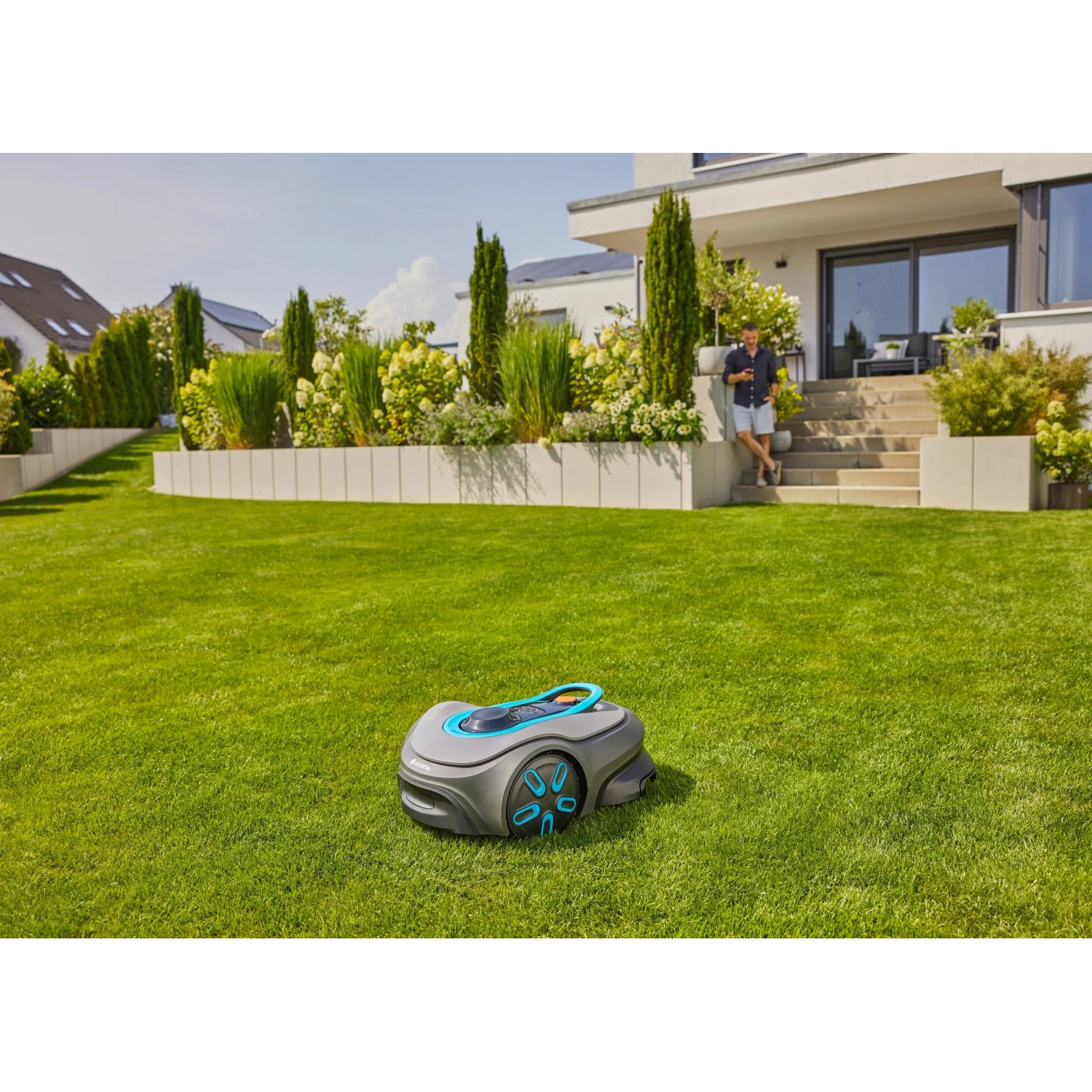 Gardena Sileno Smart Free Mähroboter auf Rasen vor Haus mit Mann. Kabelloser Rasenmäher für bis zu 600 m².