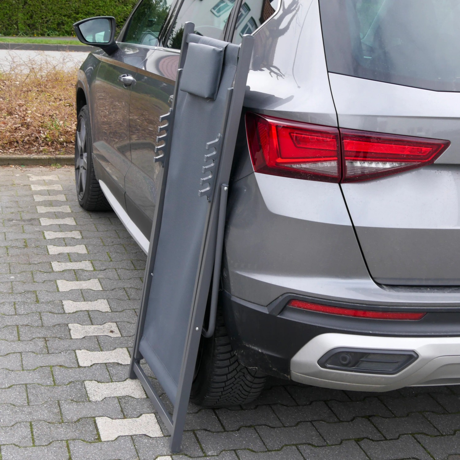 Zusammengeklappte, anthrazitfarbene FIFITARA Sonnenliege aus Metall, angelehnt an ein Auto.