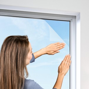 Frau befestigt weißes Windhager Fliegengitter Plus am Fenster.