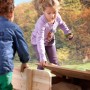 Axi Ella Sandkasten aus Holz mit Deckel und Sitzbänken, braun-grün, mit spielenden Kindern.