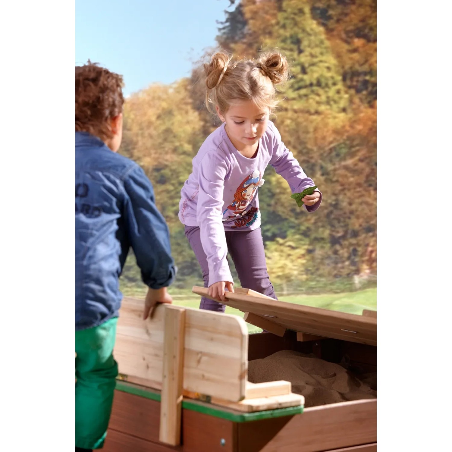 Axi Ella Sandkasten aus Holz mit Deckel und Sitzbänken, braun-grün, mit spielenden Kindern.