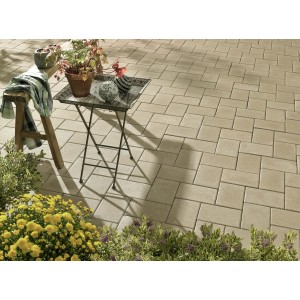 Verlegtes Betonpflaster Vero Pastellbeige (22,5x15x6 cm) auf Terrasse mit Tisch und Blumen.
