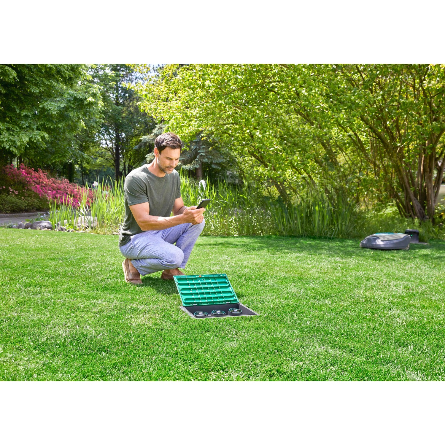 Mann bedient Gardena Bewässerungsventil 9 V Bluetooth mit dem Smartphone im Garten.
