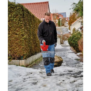 Mann streut mit dem Einhell Power X-Change Universalstreuer GE-US 18 Li-Solo Streusalz auf einen Gehweg.