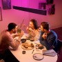 Schwarze Philips Hue Ensis LED-Pendelleuchte über Esstisch mit Personen und farbiger Beleuchtung.