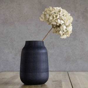 Graue Tadessi Vliestapete Urban Industrial Loft, strukturiert, als Wandhintergrund für dunkle Vase mit Blume.