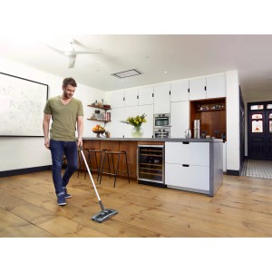 Mann reinigt Holzboden mit Black+Decker Akku-Kehrbesen. Kabelloser Bodenstaubsauger im Einsatz.