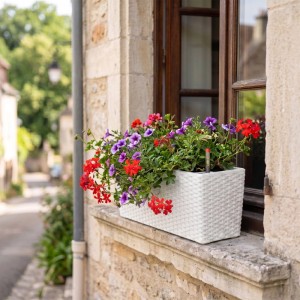 Weißer Balkonkasten aus Polypropylen in Rattan Optik mit bunten Blumen auf Fensterbank. Mit Füllstandsanzeige.