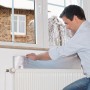 Mann montiert Tesamoll Heat Reflector Reflektierfolie hinter Heizkörper zur Wärmereflektion.
