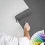 Mann streicht weiße Vliestapete mit Farbroller grau. Überstreichbare Tapete mit Struktur.
