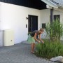 Sandbeiger 4rain Wandtank Terra 275 l am Haus mit Frau beim Gärtnern. Regentonnen zur Gartenbewässerung.