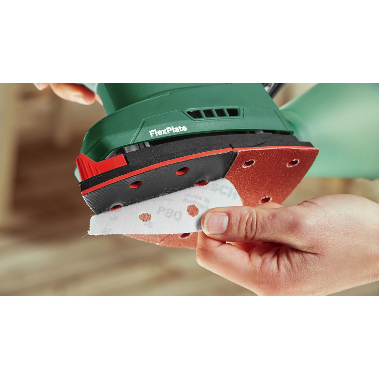 Hand befestigt Schleifpapier an roter Schleifplatte des grünen Bosch Akku-Multischleifers UniversalSander 18V-10.