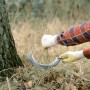Anwendung der LUX Rundsichel: Eine Person schneidet Gras mit der Sichel am Baum.