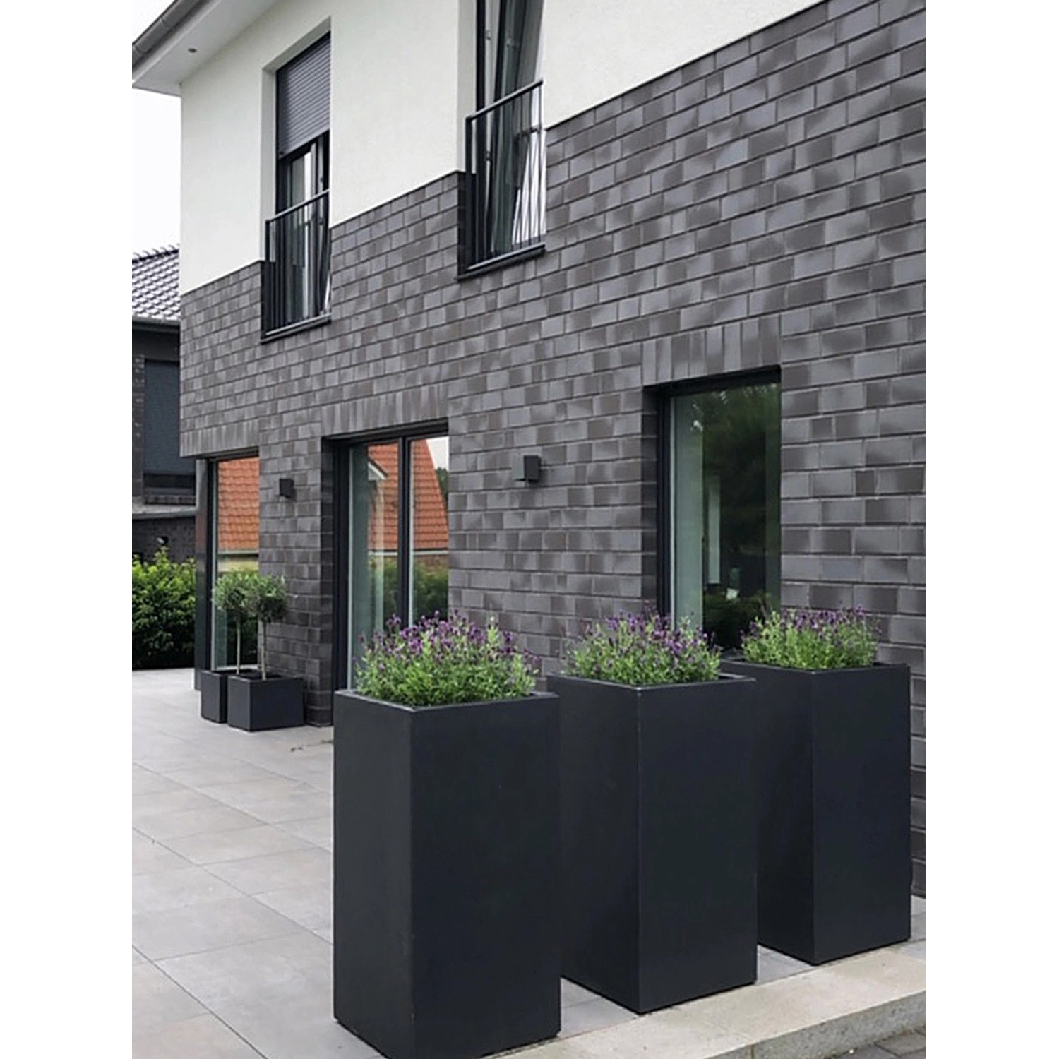 Anthrazitfarbene Pflanzwerk Tower Pflanzkübel (70 cm) vor Hauswand mit Bepflanzung.