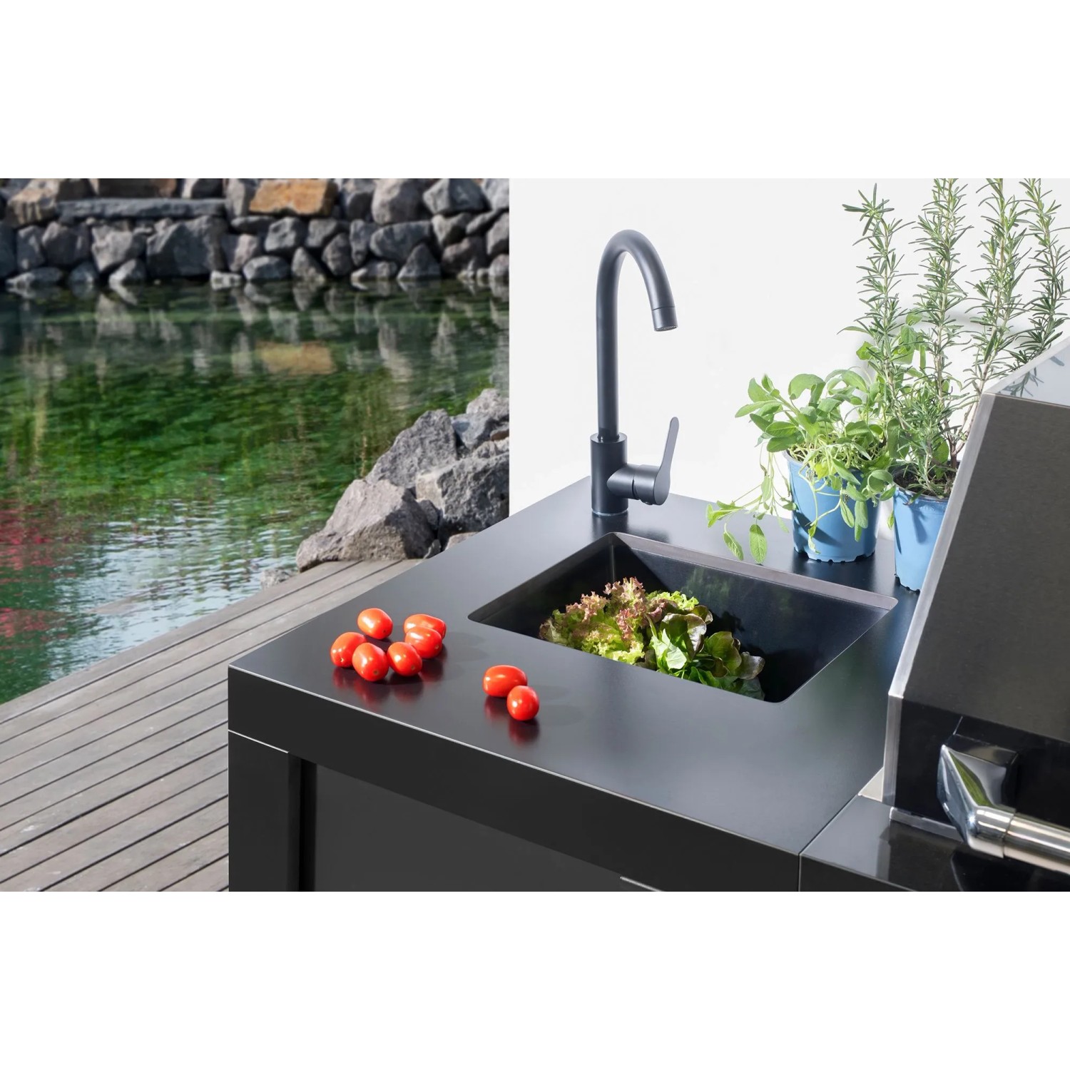 Buschbeck Outdoorküche Liverpool Schwarz mit Spüle und Armatur vor Gartenteich.