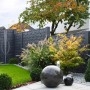 Graue Betonzaun-Platte Casa Borsika als Sichtschutz im Garten mit Pflanzen und Dekokugeln.