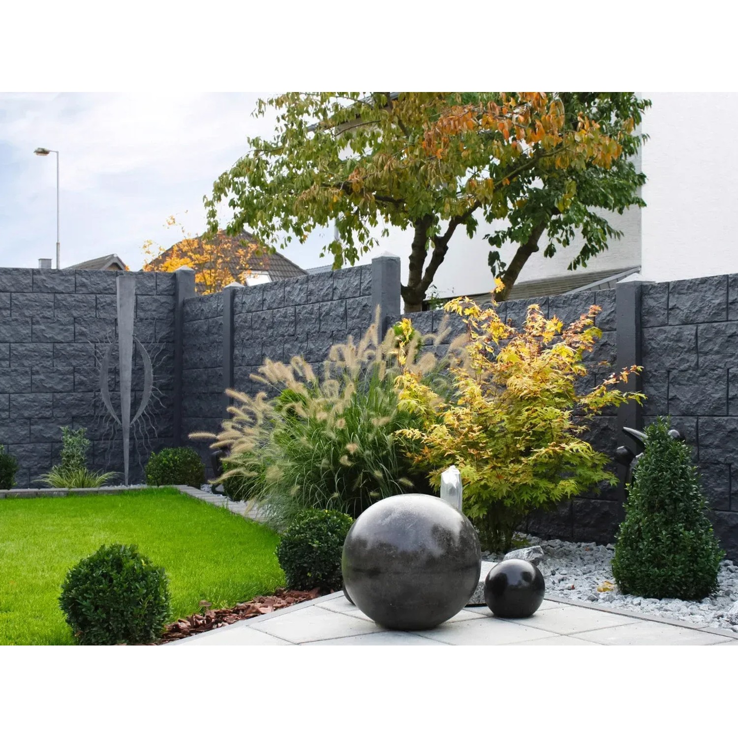Graue Betonzaun-Platte Casa Borsika als Sichtschutz im Garten mit Pflanzen und Dekokugeln.