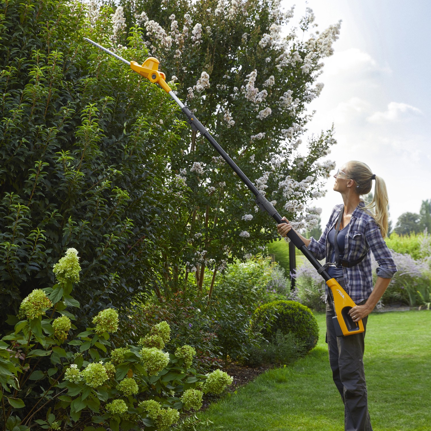 Frau schneidet Hecke mit Stiga Akku-Multitool MT 100e Akku-Heckenschere. Inkl. Akku und Ladegerät.