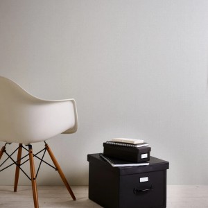Helle, graue Vliestapete in Leinenoptik von Bricoflor im Raum mit Stuhl und Boxen.