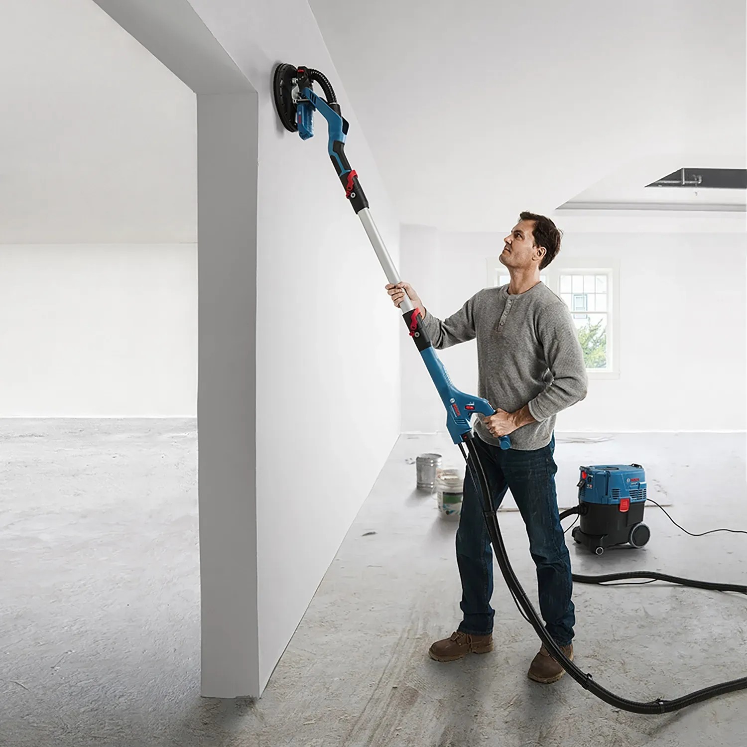 Mann schleift Wand mit Bosch Professional Trockenbauschleifer GTR 55-225. Inkl. Koffer.