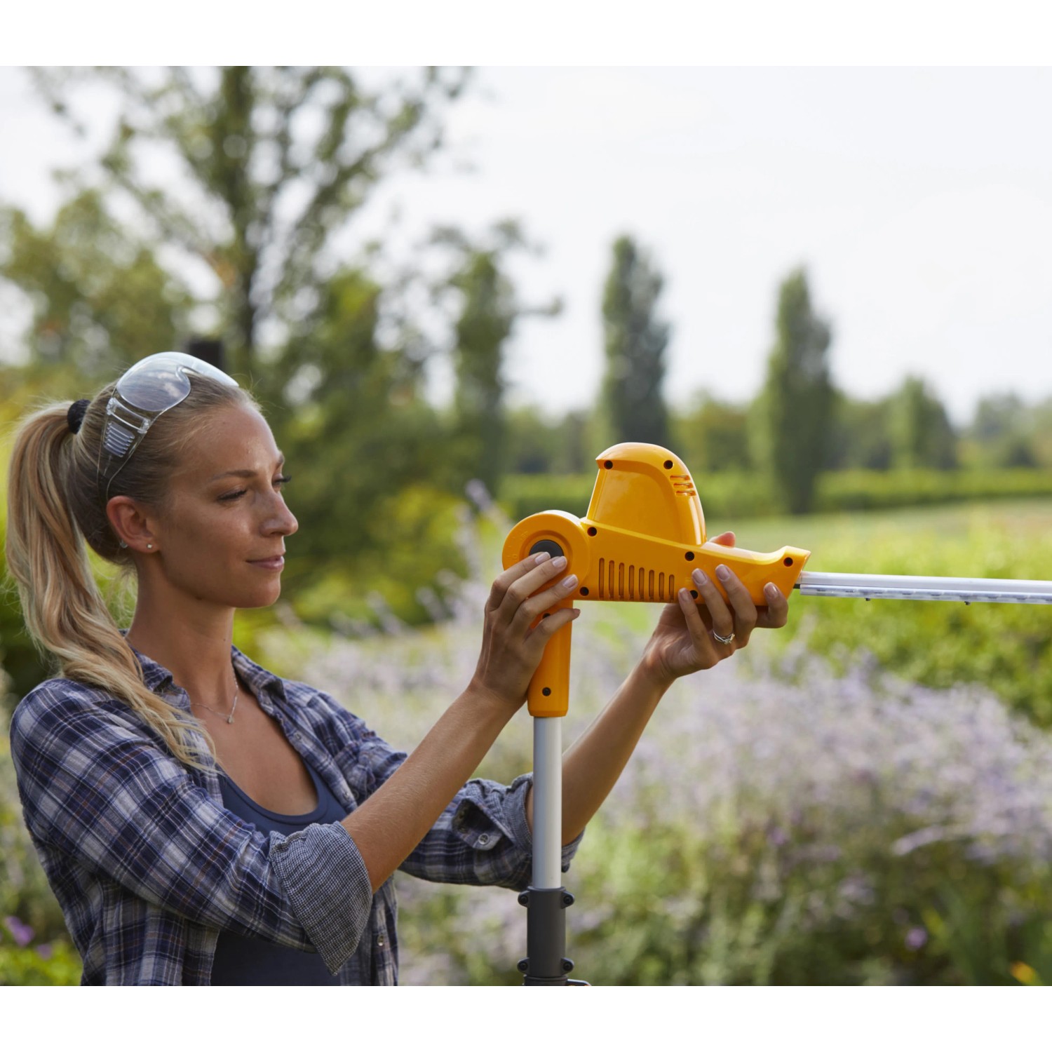 Frau bedient gelbes Stiga Akku-Multitool MT 100e. Akku-Heckenschere mit Teleskopstiel.