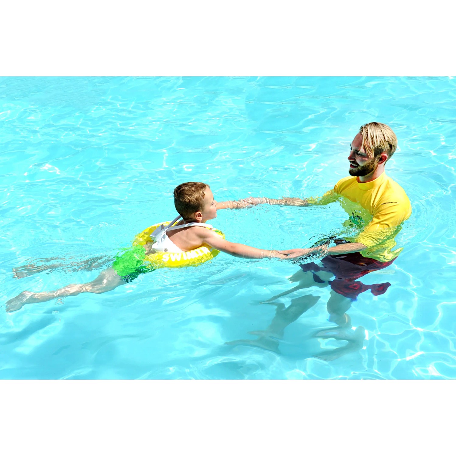 Kind mit gelbem Freds Swim Academy Schwimmreifen im Pool, unterstützt von einem Erwachsenen.