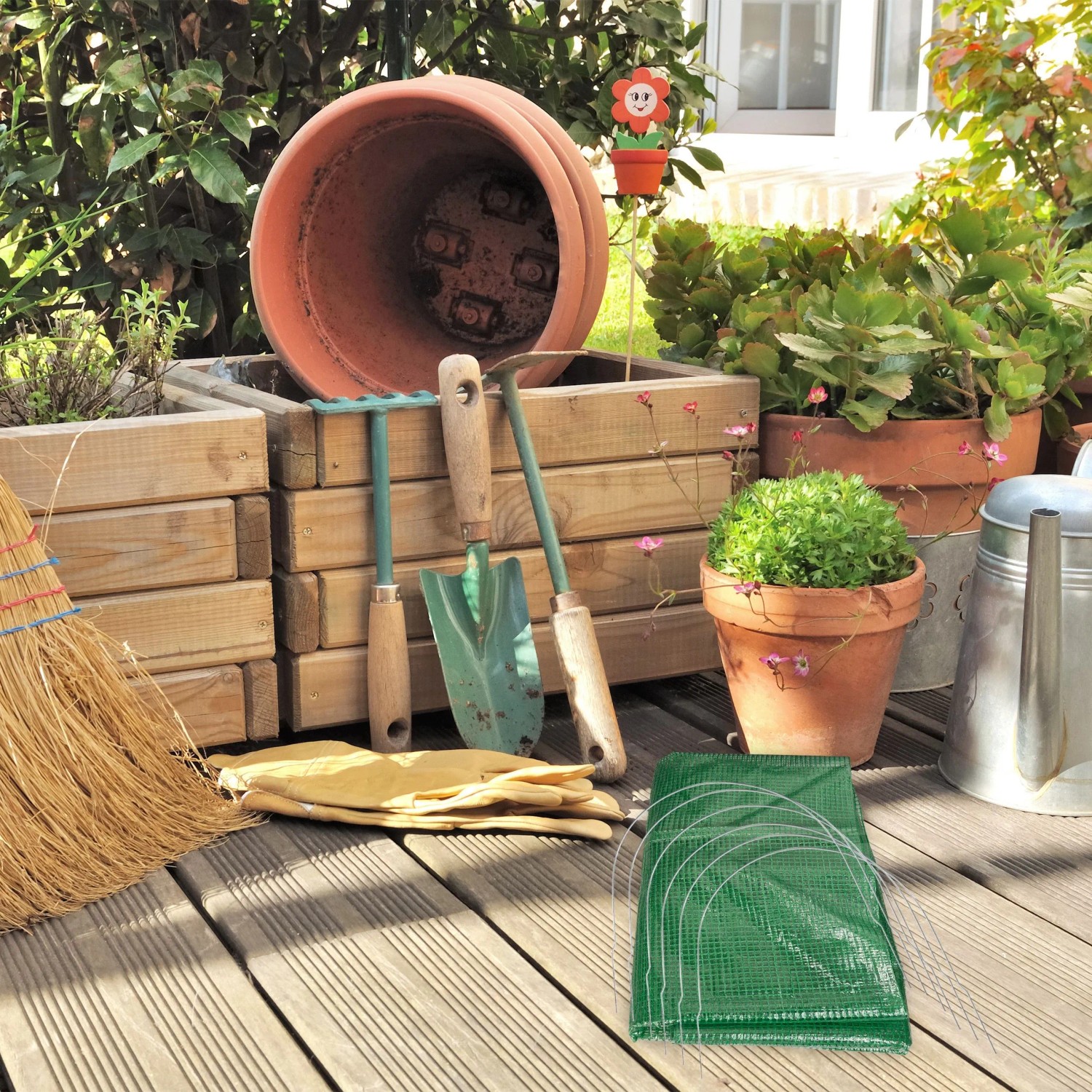 Gefalteter Relaxdays Pflanztunnel grün/transparent aus PVC und Stahl auf Holzterrasse mit Gartenzubehör.