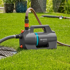 Gardena Gartenpumpe 5200 Silent im Einsatz auf Rasen. Graue Pumpe mit blauem Akzent und angeschlossenen Schläuchen.