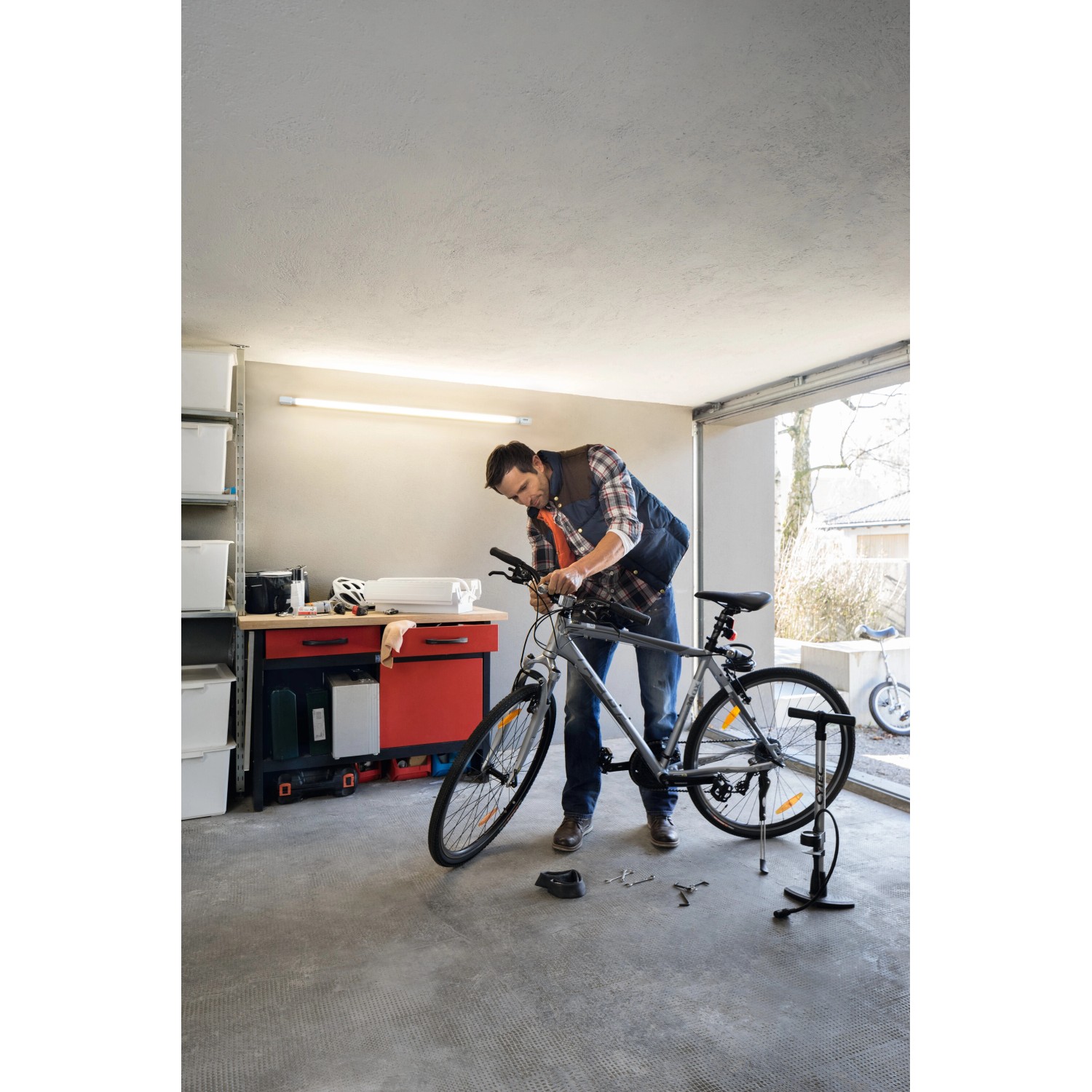 Mann repariert Fahrrad unter Osram LED-Leuchtstofflampe in Garage. Warmweißes Licht.