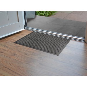 Anthrazitfarbene Sauberlaufmatte Stirling 60x80 cm vor einer Tür auf Holzboden.