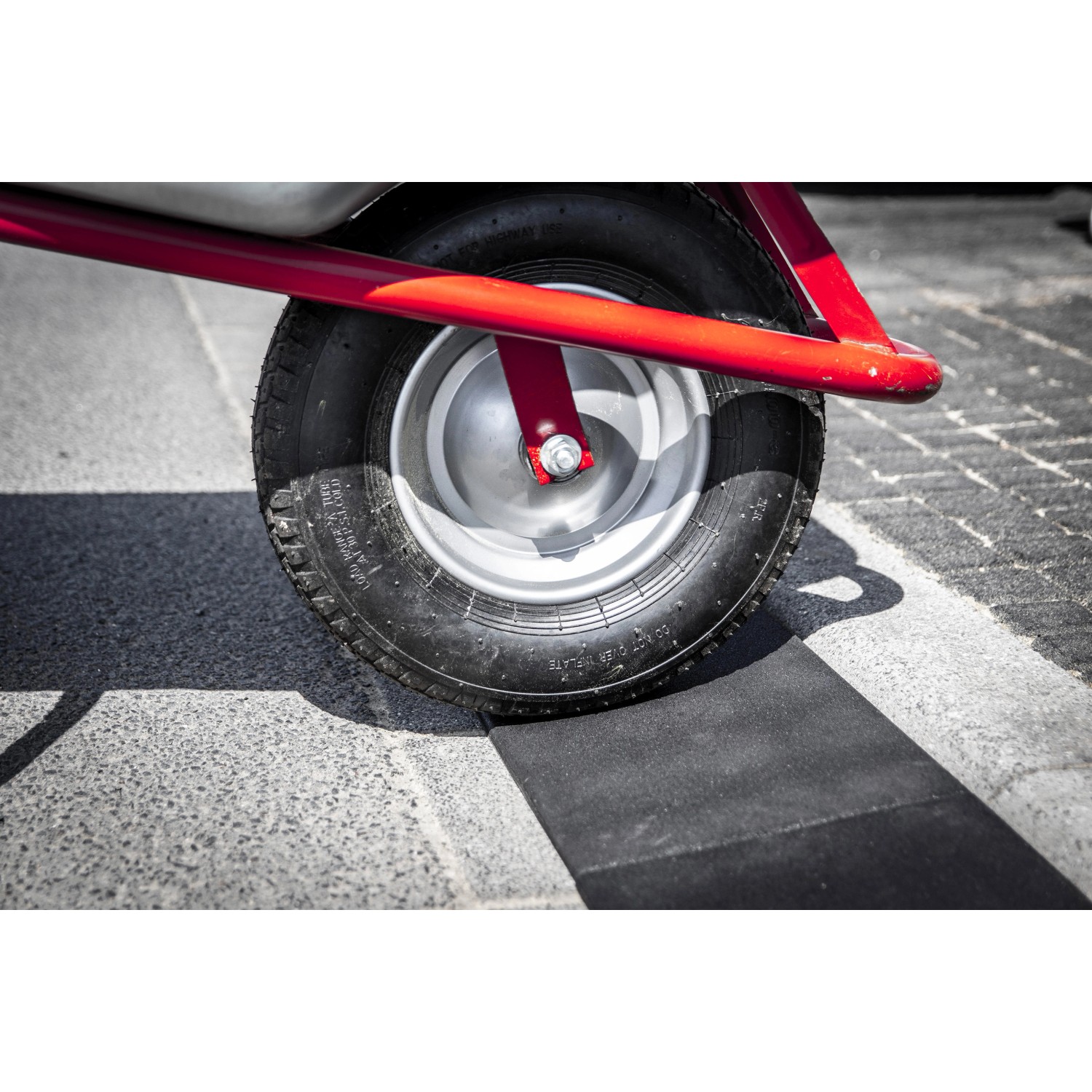 Rad überfährt schwarze Bordsteinrampe (1000x250x7-45mm) auf Pflaster.