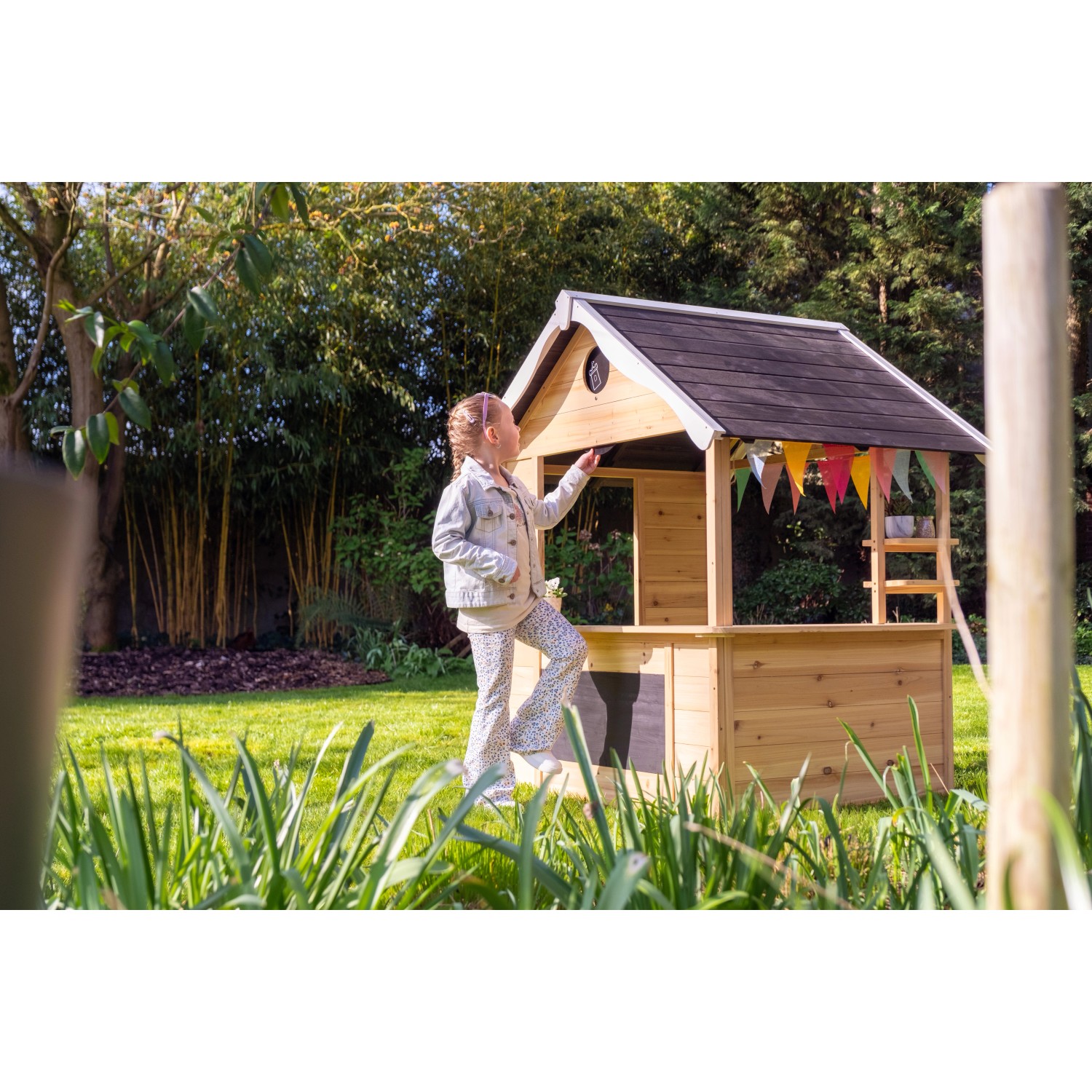 Kind spielt am Exit Holzspielhaus Hika mit Theke und Rollenspiel-Rad im Garten.