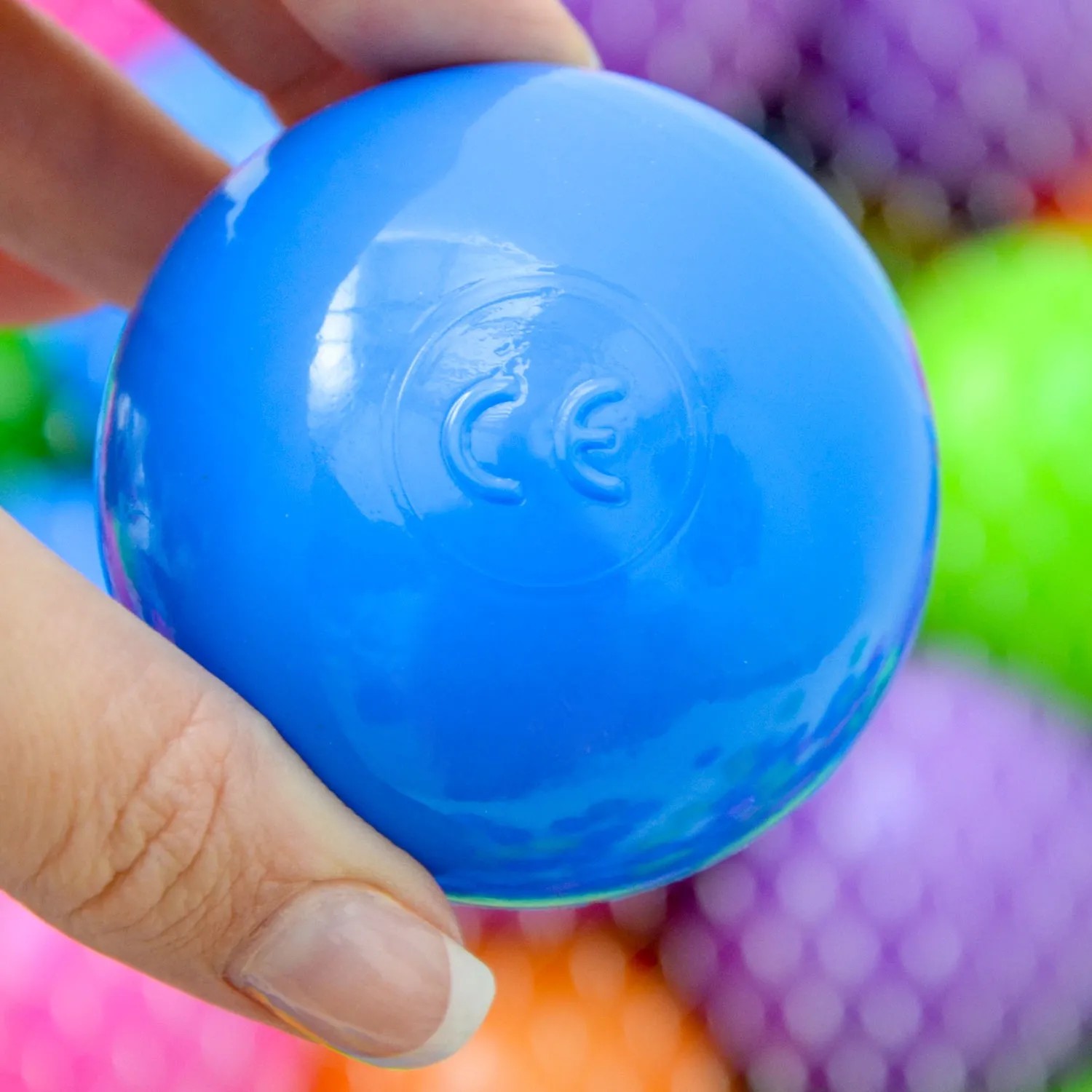 Blauer LittleTom Bällebadball (Ø 6 cm) mit CE-Kennzeichen in Hand, Pastellfarben im Hintergrund.